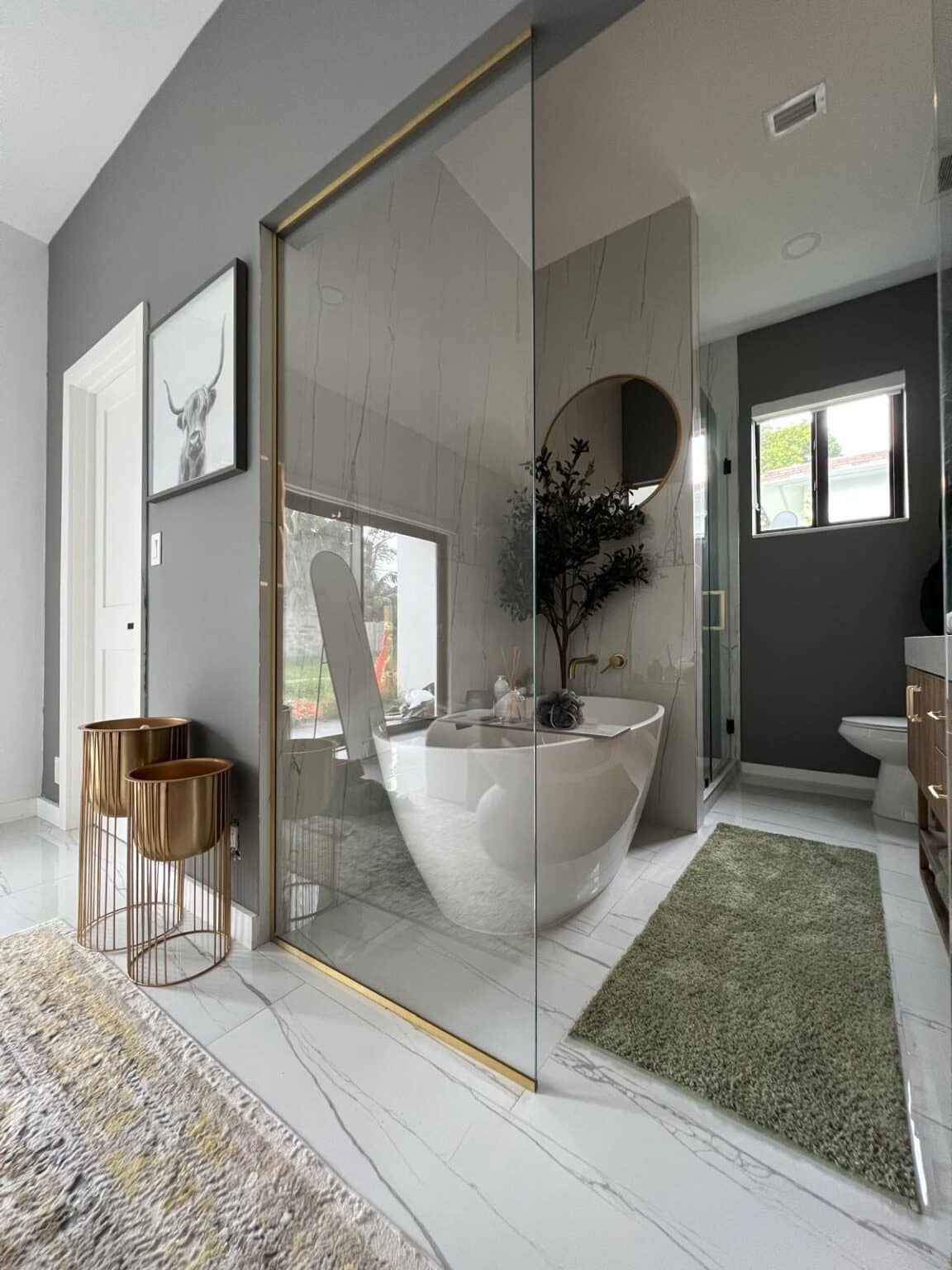 Bathroom with a gold-framed glass partition, a freestanding tub and a round mirror