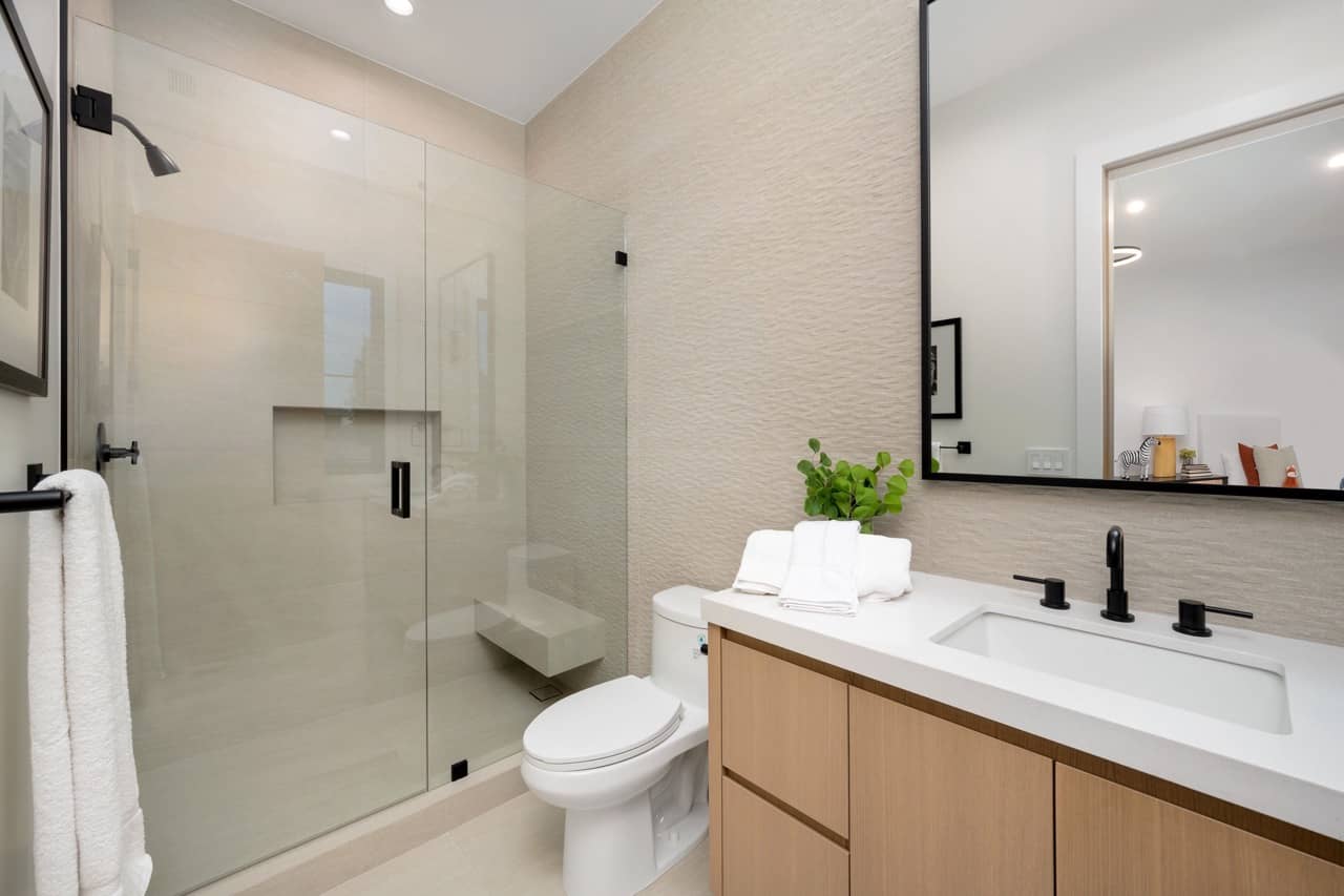 Glass walk-in shower beside a wood vanity with a white top