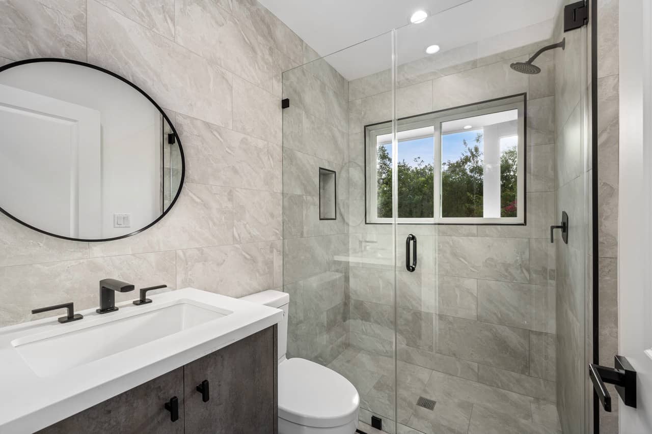 Bathroom with gray stone-look tile, a round mirror and a glass shower