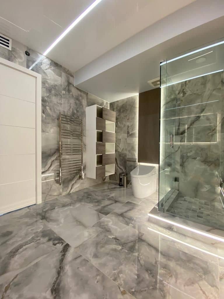 Marble-look bathroom with a glass shower, a heated towel rack and LED cove lighting