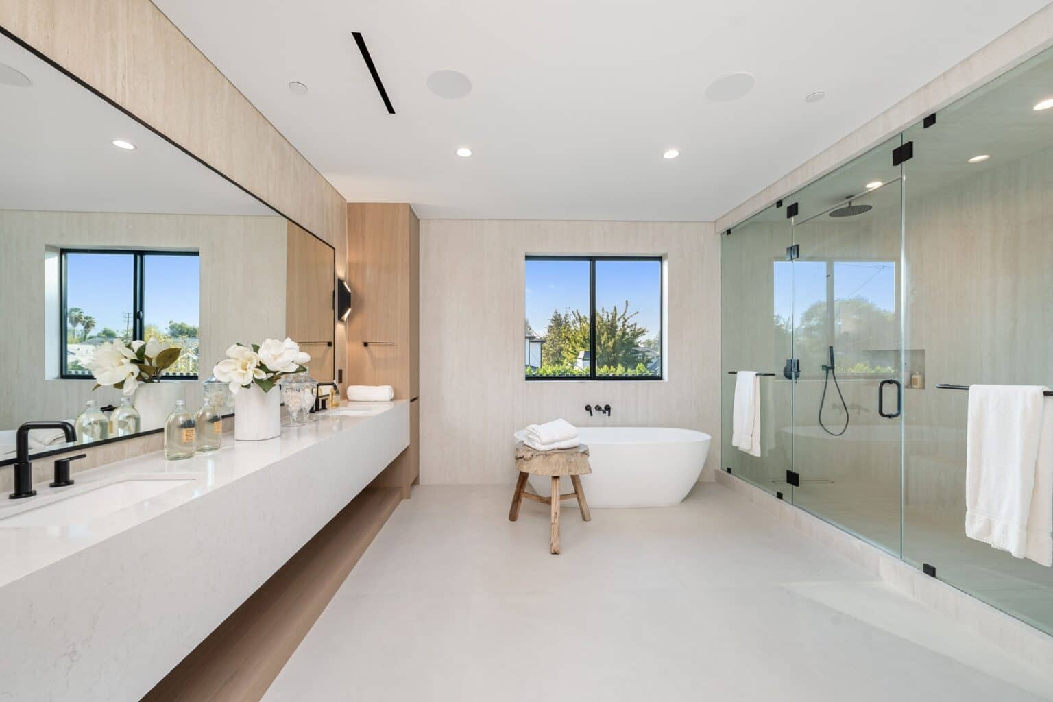 Minimal white bathroom with a long floating vanity, a freestanding tub and a glass shower