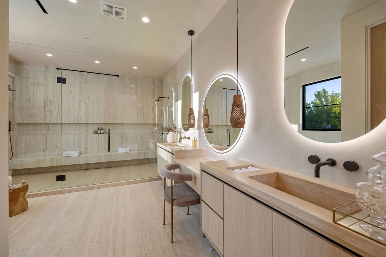 Bathroom with round backlit mirrors, a stone vanity and a glass shower