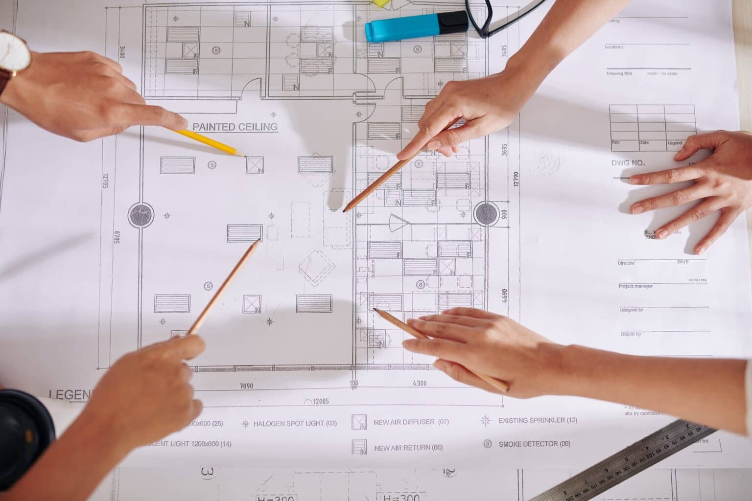 Hands with pencils and a ruler going over a floor plan