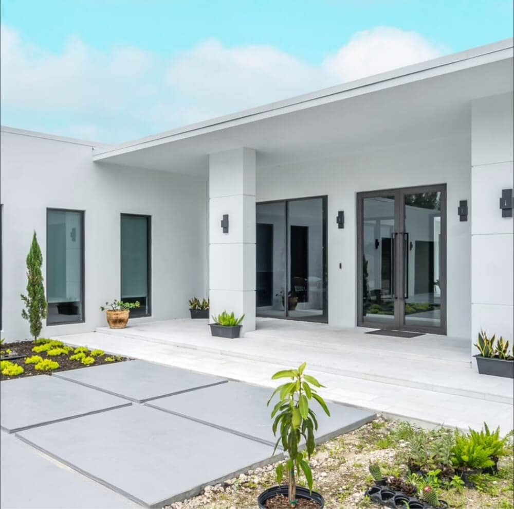 Modern white South Florida home with dark-framed impact glass entry doors and tall impact windows