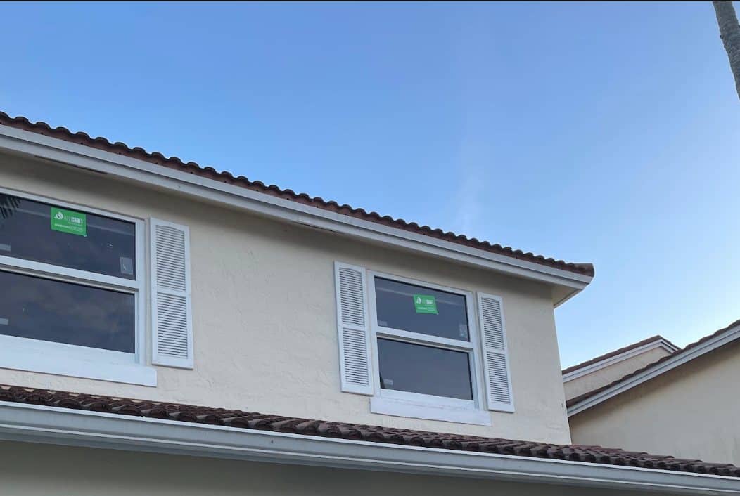 Two new impact windows, labels still on the glass, on a two-story home with a clay barrel tile roof