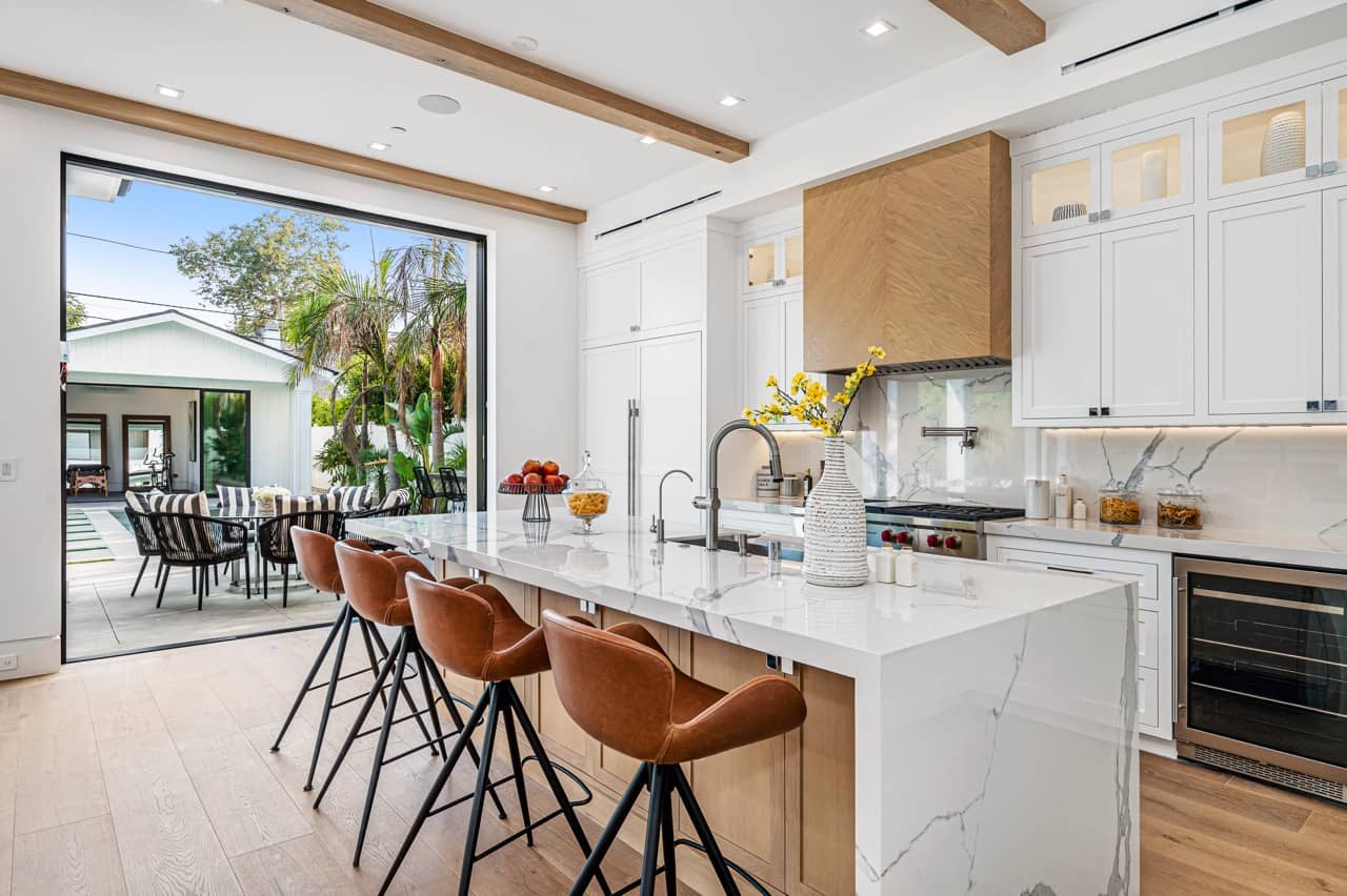 Bright kitchen with a white stone island, leather counter stools and glass doors open to the patio