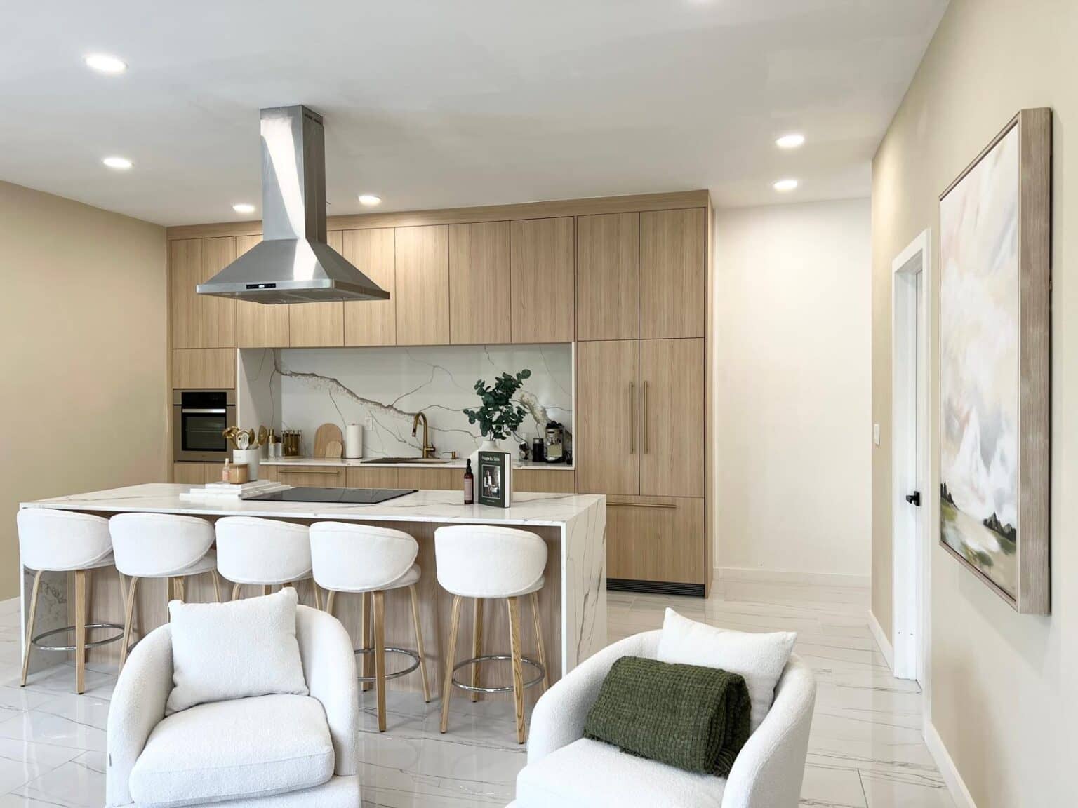 Light wood kitchen with a white island, counter stools and a stainless steel range hood