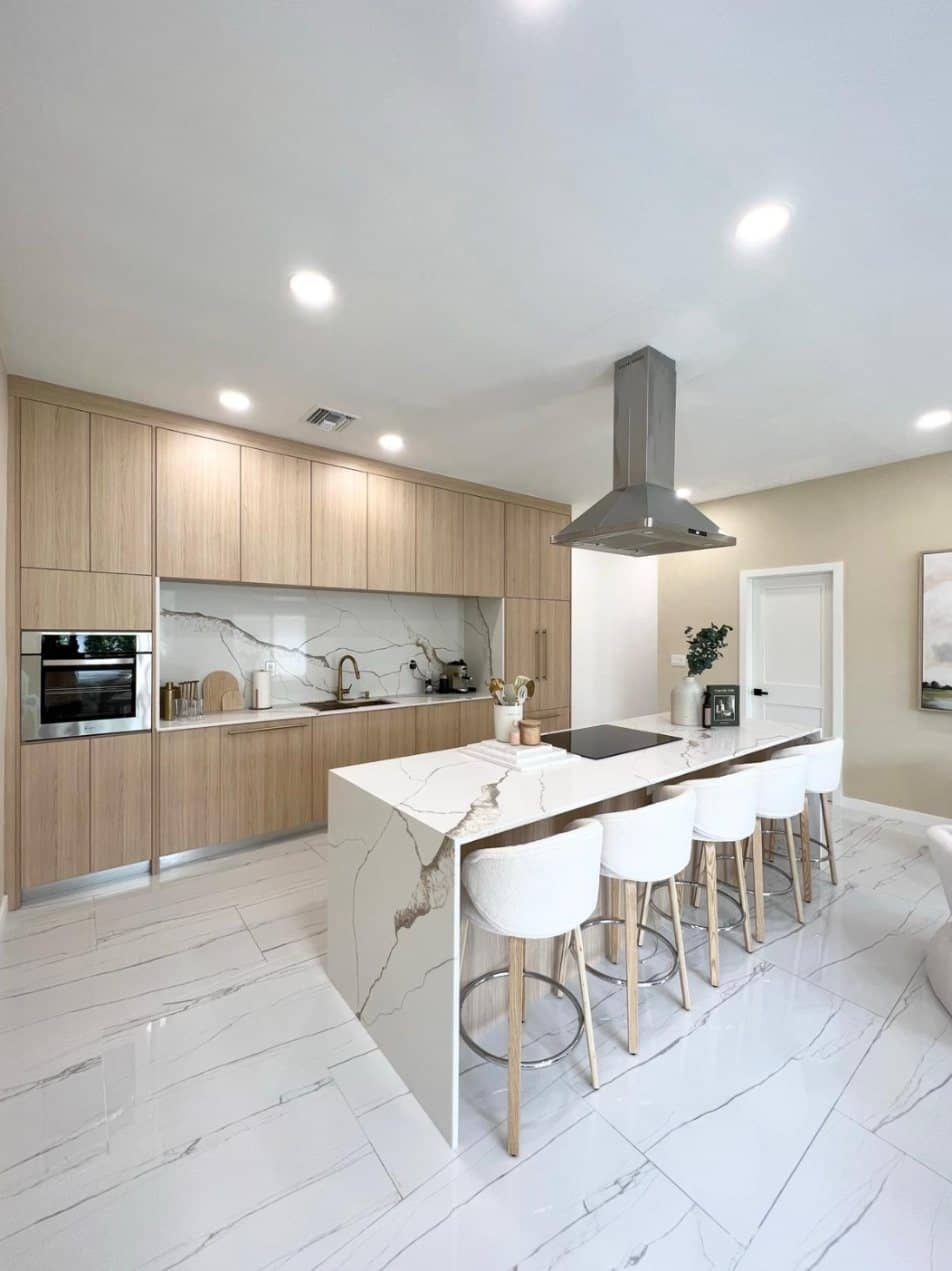 Kitchen remodeled by Novara with light wood cabinets, a white marble waterfall island and white bar stools