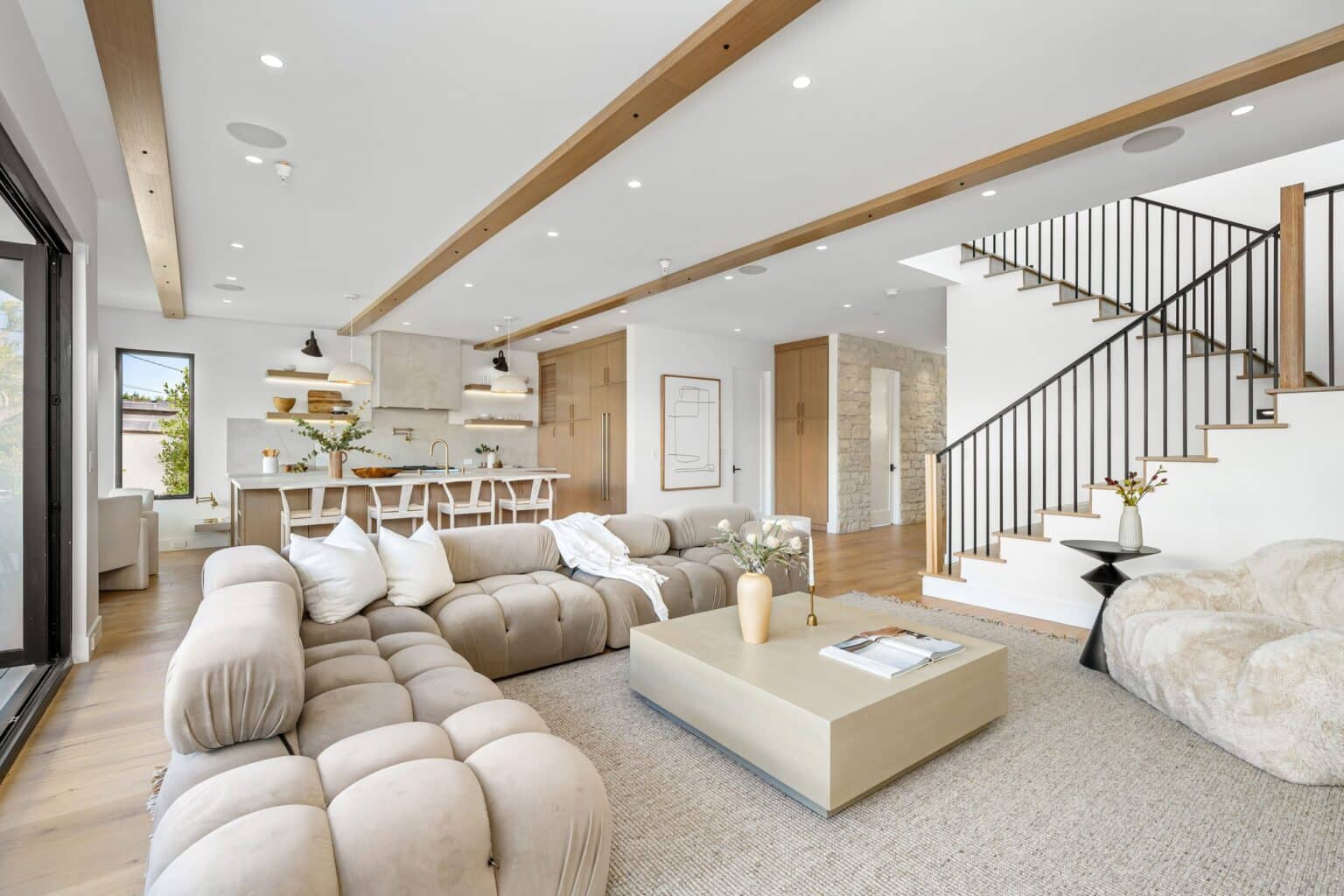 Bright open-concept living room with wood ceiling beams and a view into the kitchen