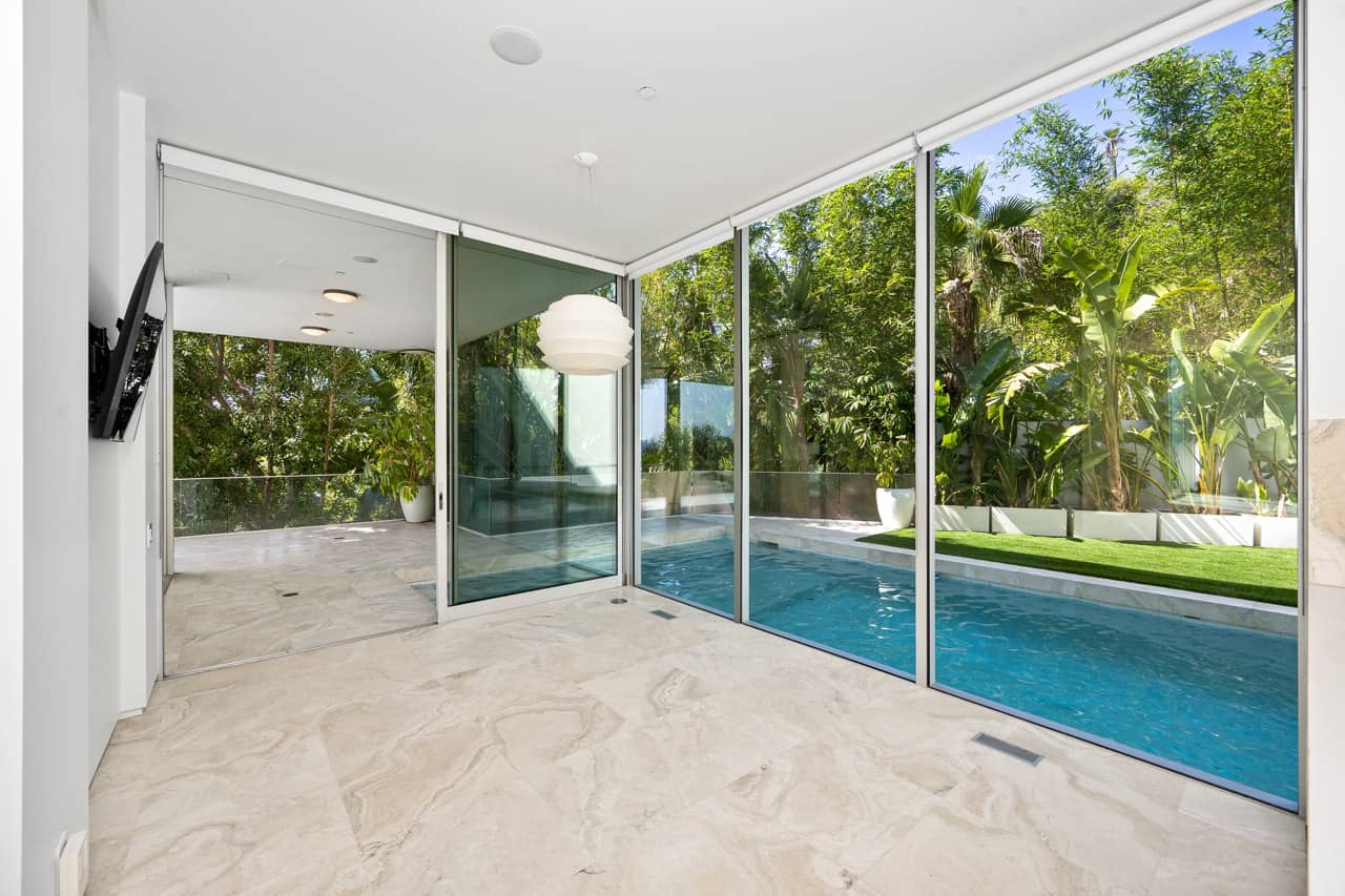 Covered patio with glass walls beside an in-ground pool