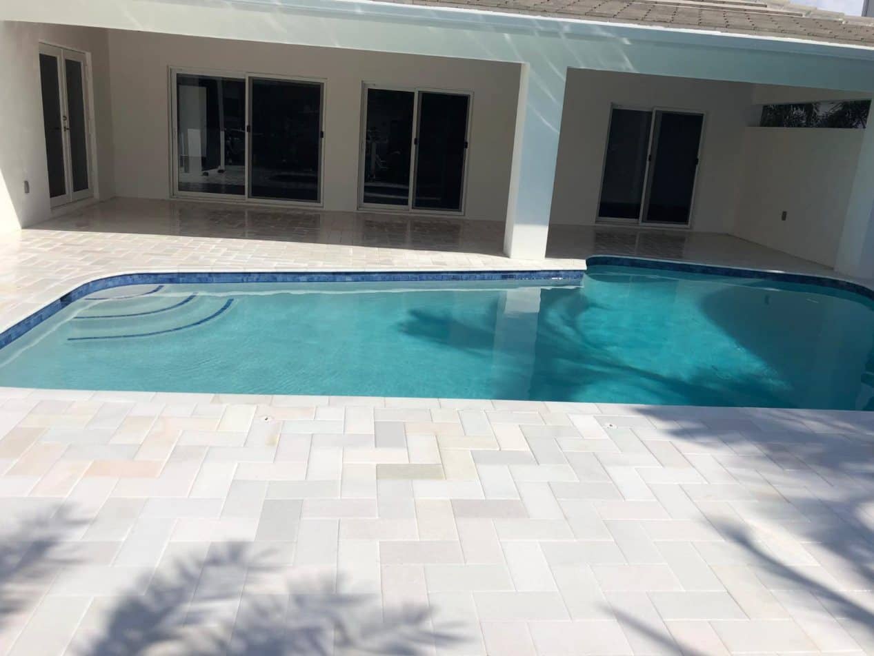 New pool with a light paver deck behind a South Florida home