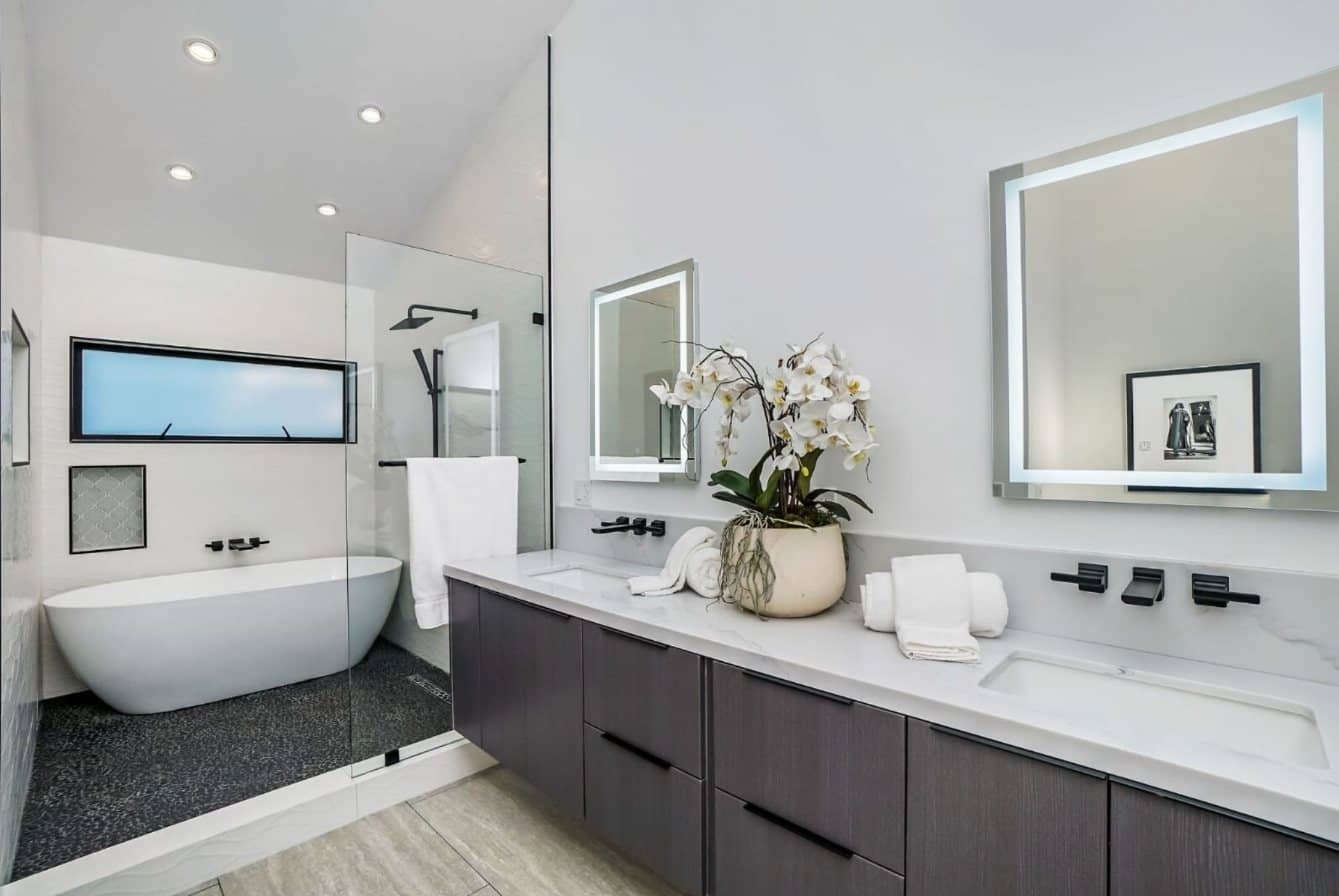 Primary bathroom remodeled by Novara with a freestanding tub, glass walk-in shower and a double vanity with backlit mirrors