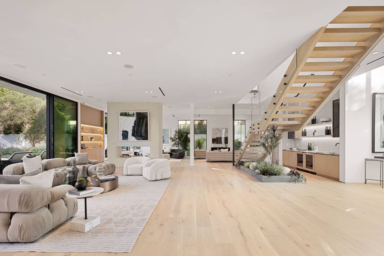 Living room with a wood staircase, light wood floors and large windows