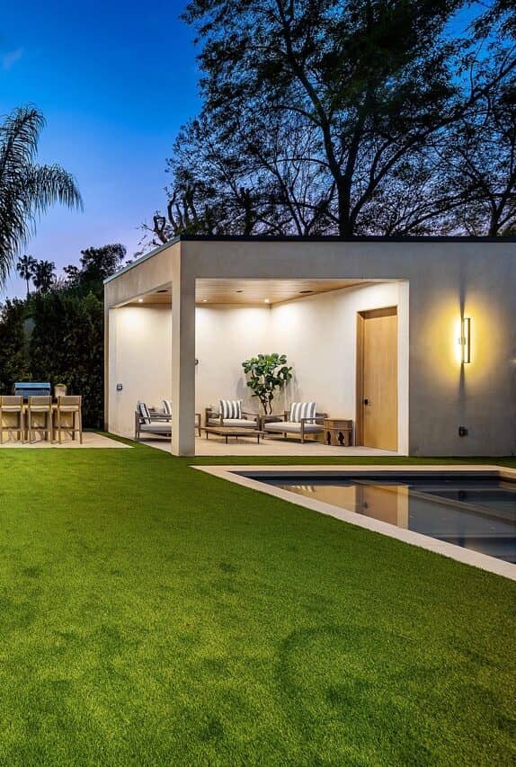 Pool house with a lit patio and a lawn at dusk